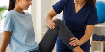 A physical therapist assisting a woman with a leg exercise in a clinical setting.
